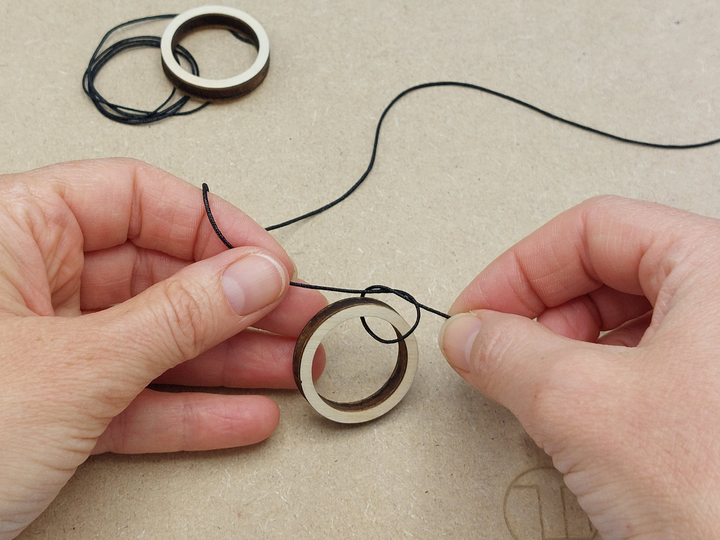 Het vastknopen van het zwarte touwtje aan een houten ring bij Gatengekte; stap-voor-stap DIY knutselen, geschikt voor kinderfeestjes.